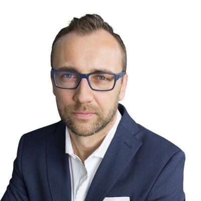 Man with glasses and beard wearing a blue suit against a white background.